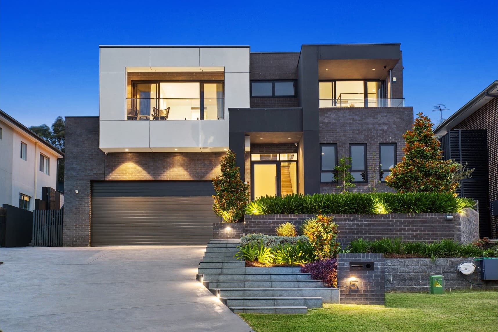 A newly built contemporary brick home at dusk with warm interior lighting.